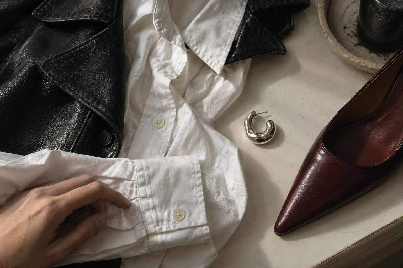 Close-up of a cotton cuff, textured leather lapel, silver earring and oxblood shoe